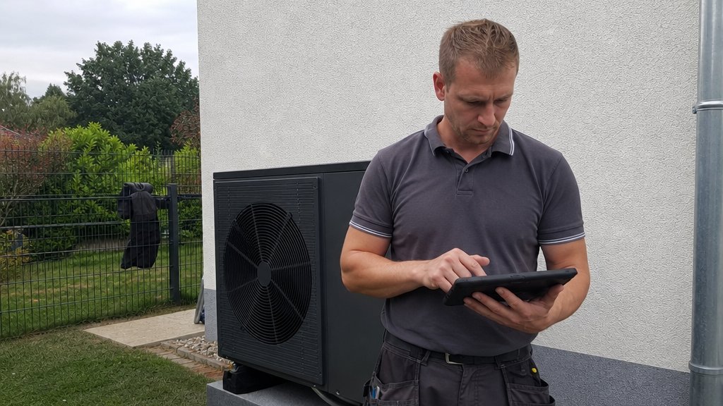 Heizungsbauer mit Tablet vor einer installierten Wärmepumpe
